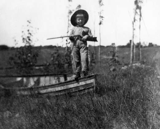 Young Ernest Hemingway holds a gun while standing on a boat, near Windemere Cottage at Walloon Lake, MI, summer 1903. Please credit: "Ernest Hemingway Collection/John F. Kennedy Presidential Library and Museum, Boston.